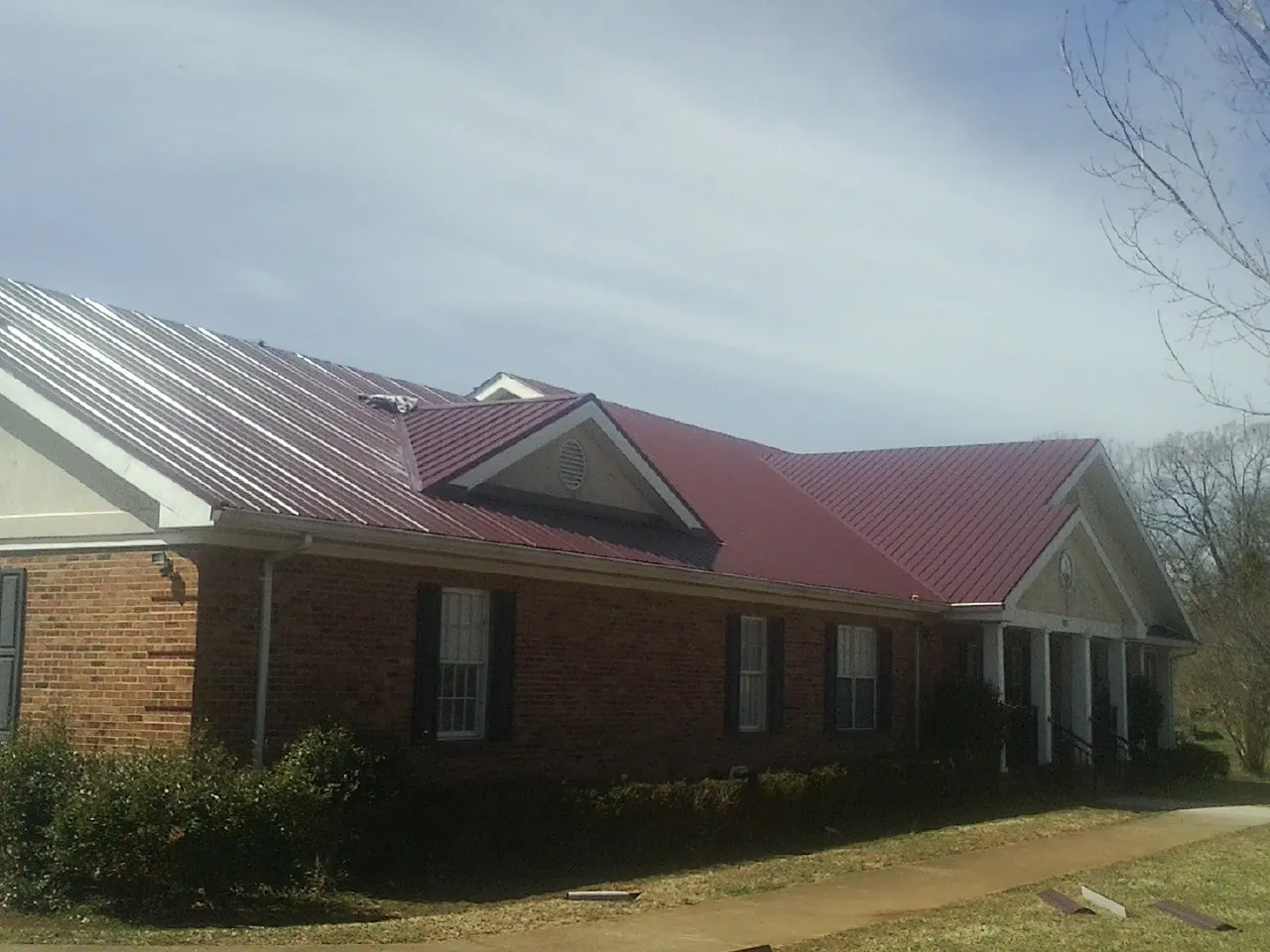 Red metal roof with gabled entries on a long brick building, from a Hail Damage Roof Repair job in Cape May Court House
