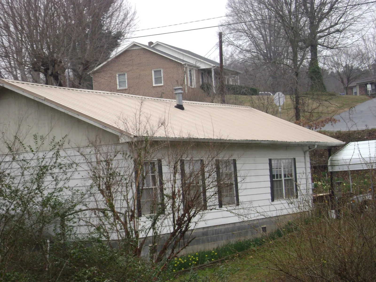 Tan metal roof on a white sided house set into a hillside — Commercial Roofing by Roofing Brothers in Cape May Court House